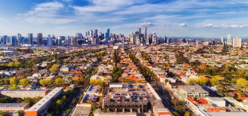 Aerial view of Melbourne city CBD high-rise towers from Port Melbourne and Southbank above residential suburb house roofs and local streets, roads, cars and parks.